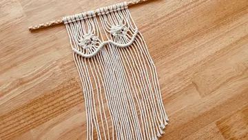 Macrame wall hanging with fringes on wood surface