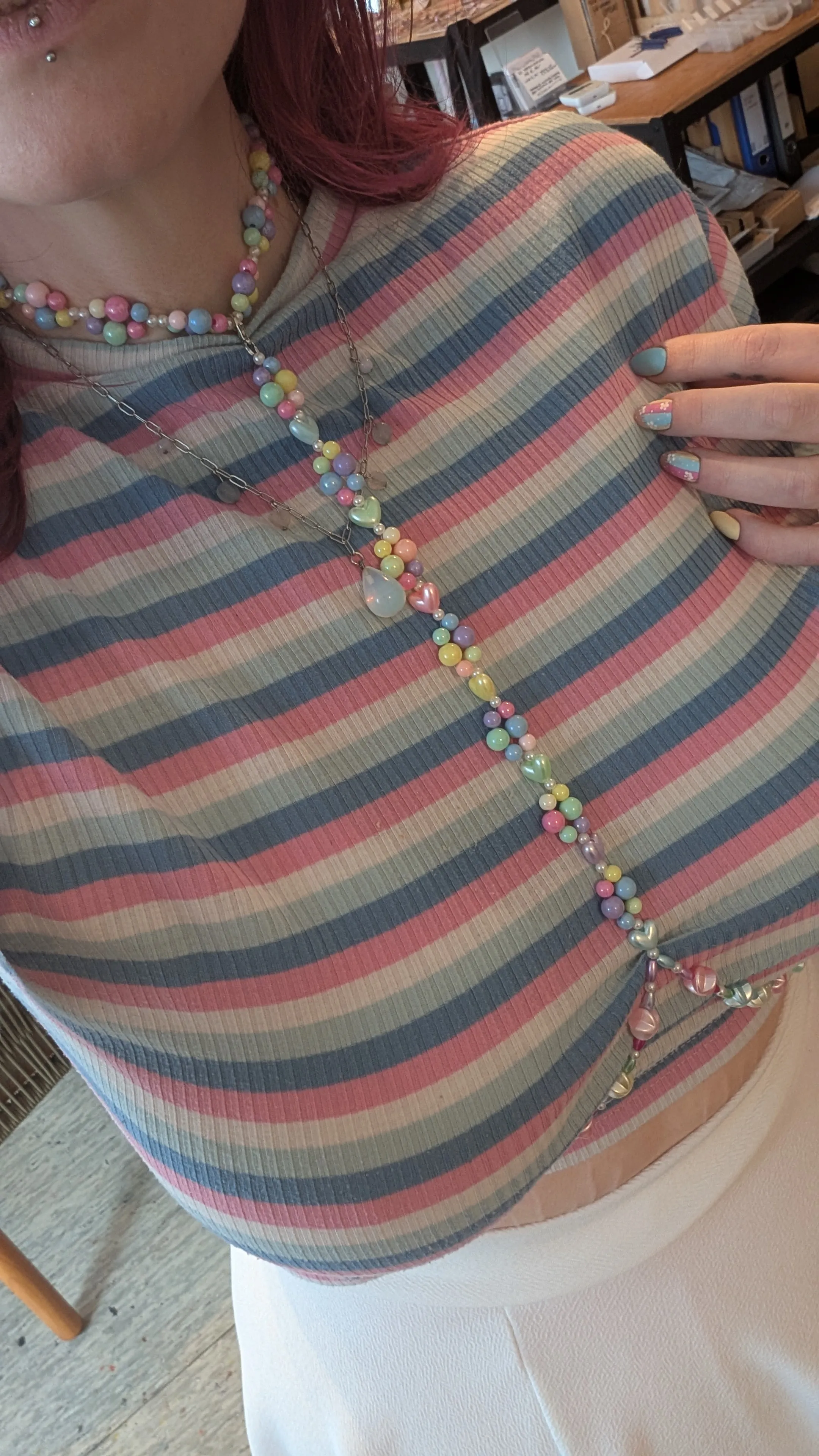 Person trägt gestreiftes Oberteil, bunte Perlenkette.