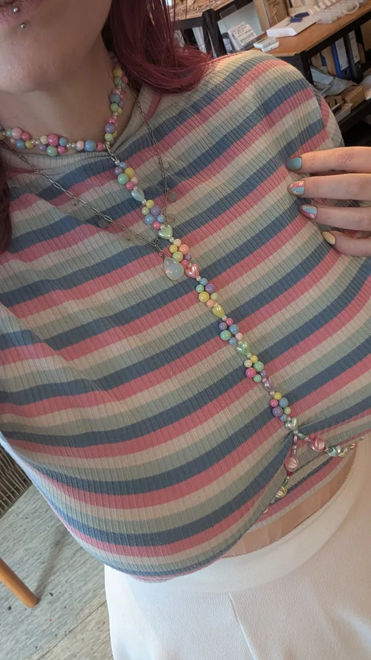 Person trägt gestreiftes Oberteil, bunte Perlenkette.
