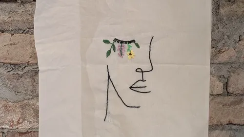 Line art face with embroidered flowers, brick wall.