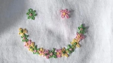 Blumengesticktes Smiley auf weißem Stoff.