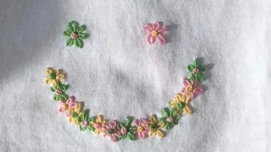 Flower embroidered smiley on white fabric.