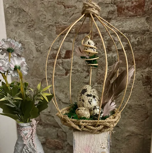 Decorative birdcage with eggs and feathers inside.