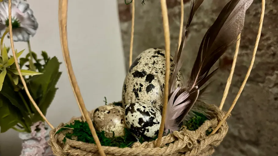 Gesprenkelte Eier mit Federn im Korb.