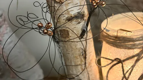 Drahtblume an Birkenast neben beleuchteter Kerze.