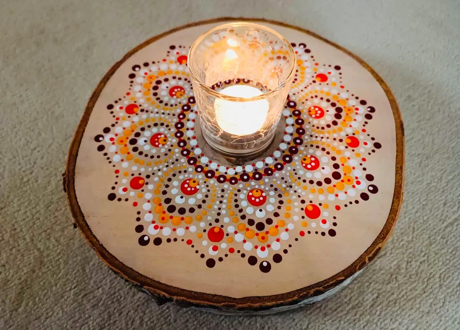 Candle on painted wood slice, colorful dots decor.