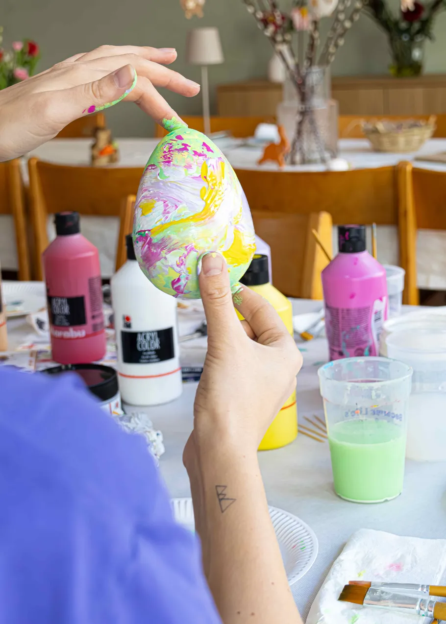 Person painting colorful egg at table.