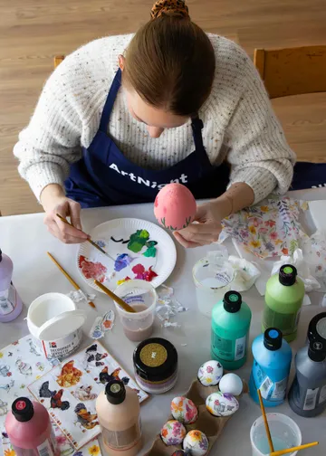 Person painting egg at table with paints.
