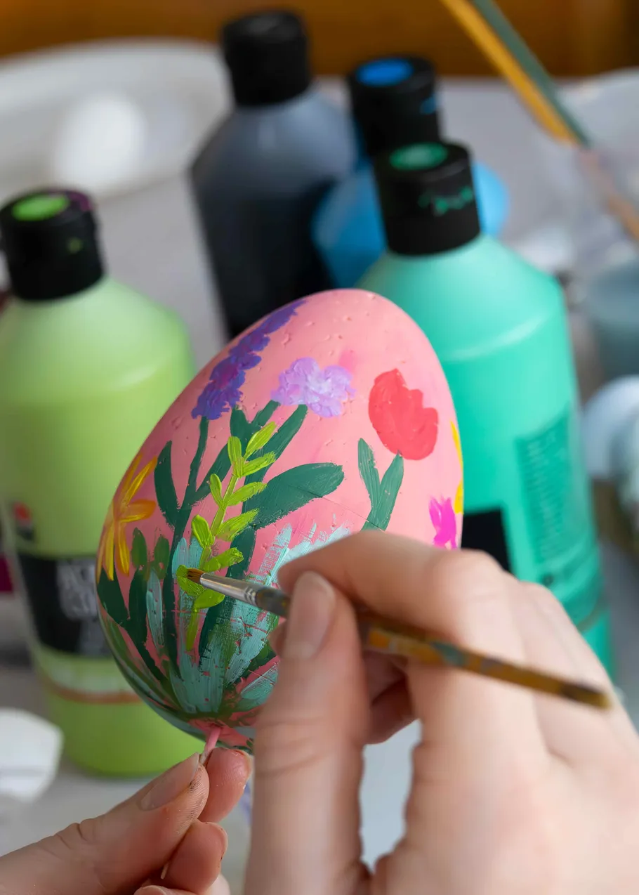 Hand paints flowers on pink egg.