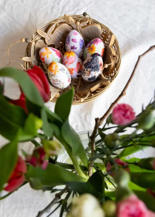 Decorated Easter eggs in basket, flowers in foreground.
