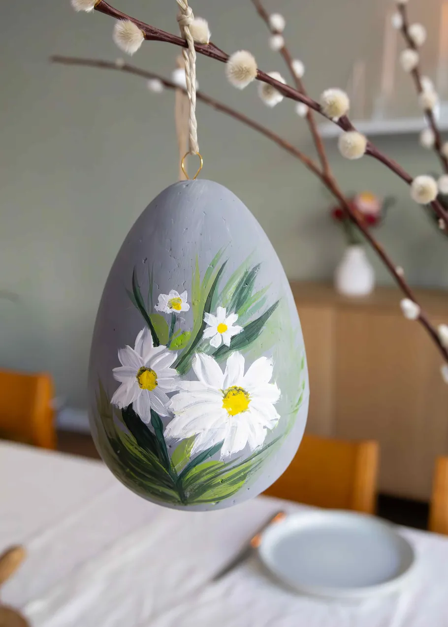 Painted egg hanging from branch above table.