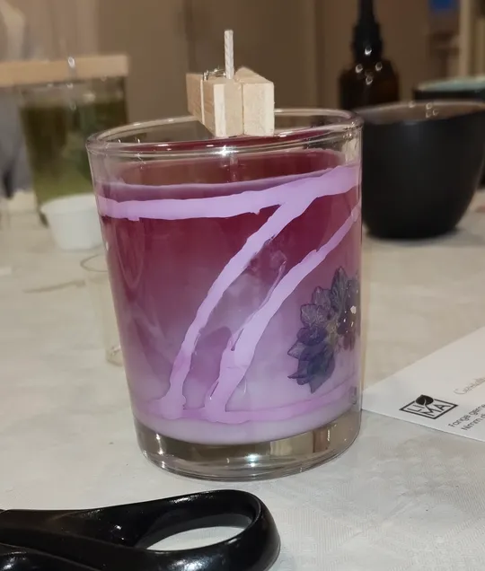 Glaskerze mit lila Wachs auf Tisch.