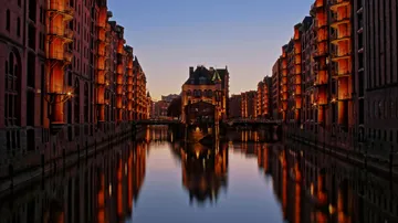 Beleuchteter Kanal mit Gebäuden bei Dämmerung.