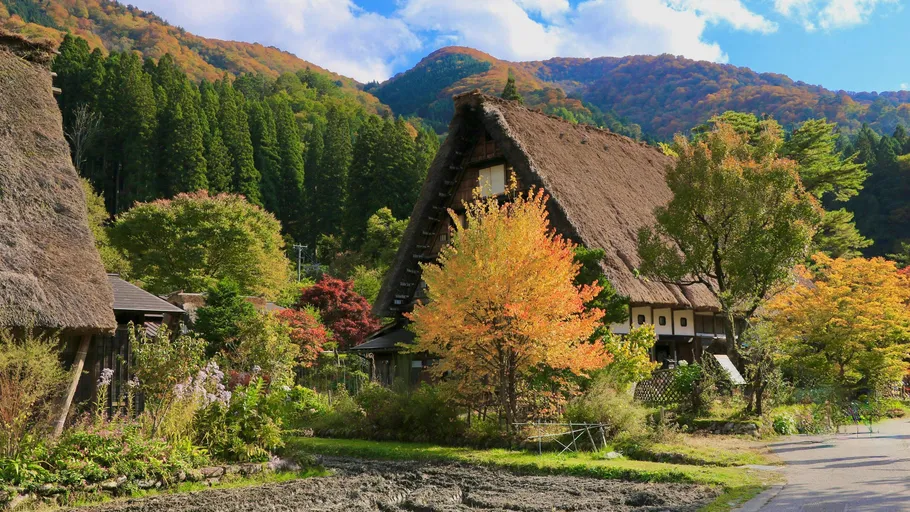Traditional thatched house amid autumn trees and mountains.