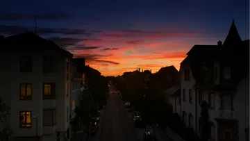 Sonnenuntergang über ruhiger Straße mit Gebäude-Silhouetten.