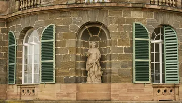 Stone statue between green-shuttered windows.