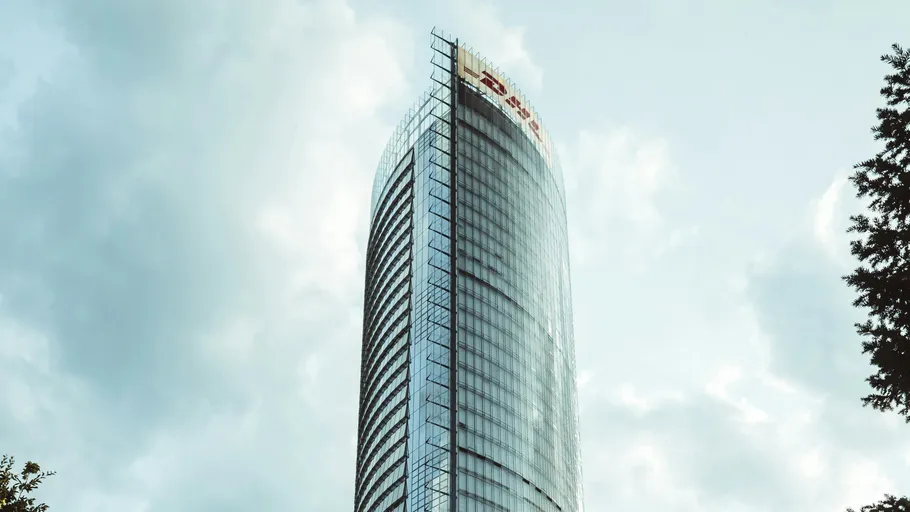 Tall glass skyscraper under cloudy sky.