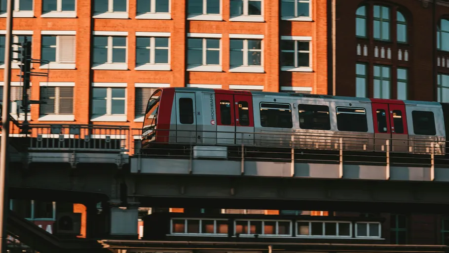 Train moving on elevated track, city buildings behind.