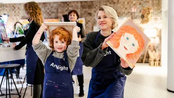 Child and woman showing paintings at event.