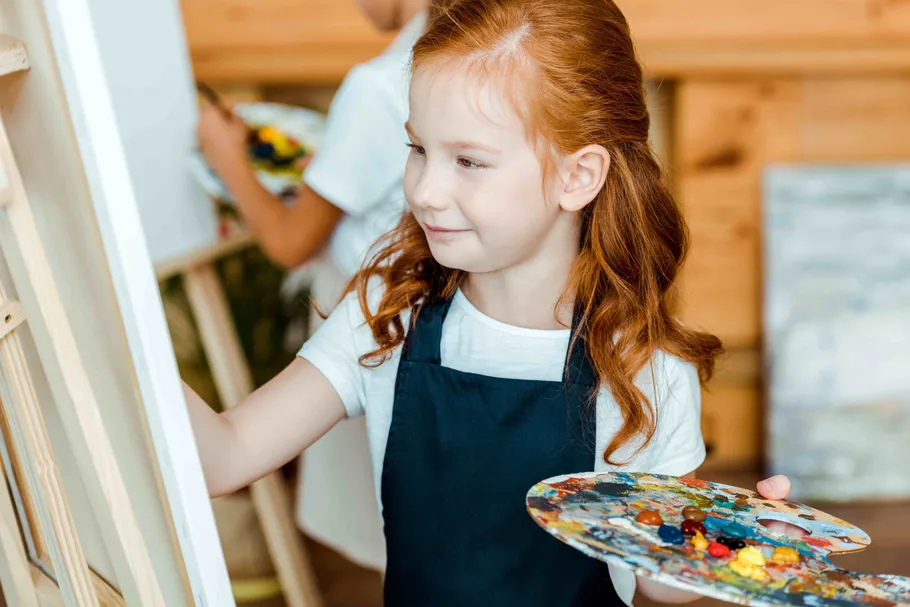 Girl painting on canvas holding palette in studio.