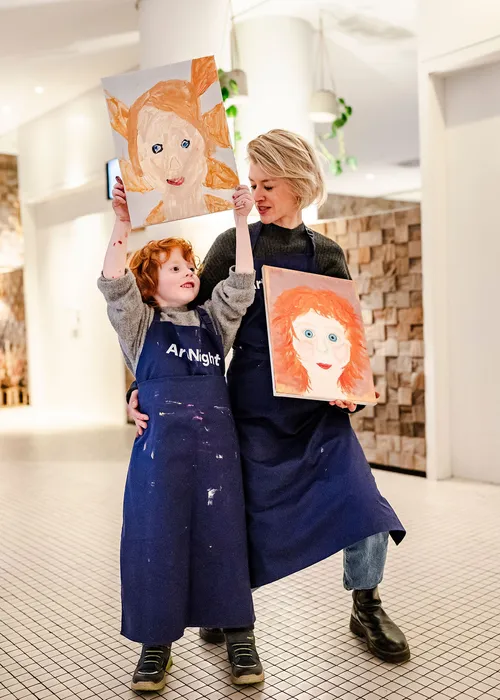 Child and adult hold paintings in art studio.