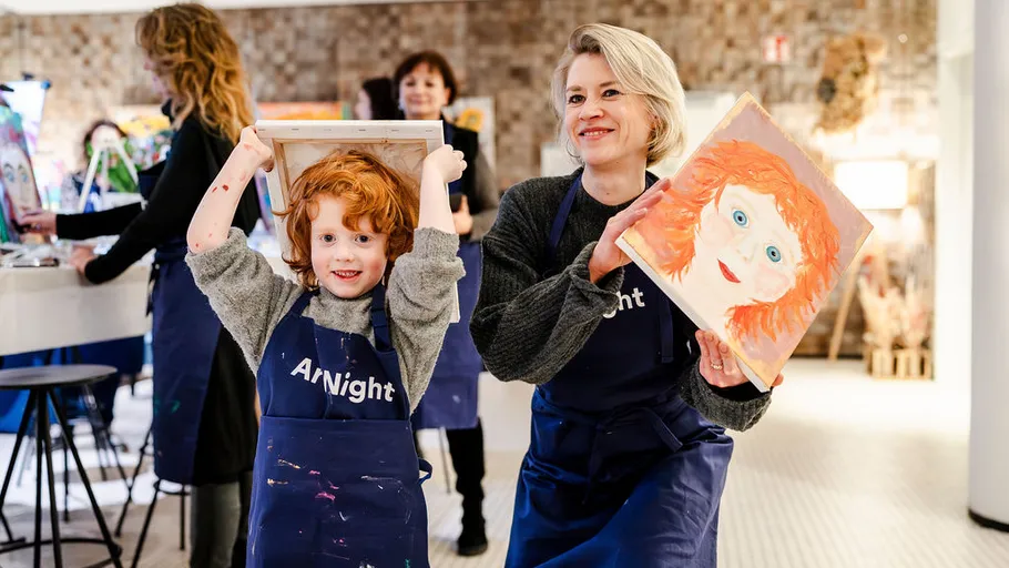 Child and adult showing paintings, indoor workshop.