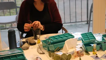 Person arrangiert Blumen an einem Tisch drinnen.