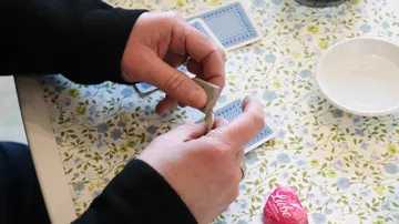 Hands shuffling cards at floral-patterned table.