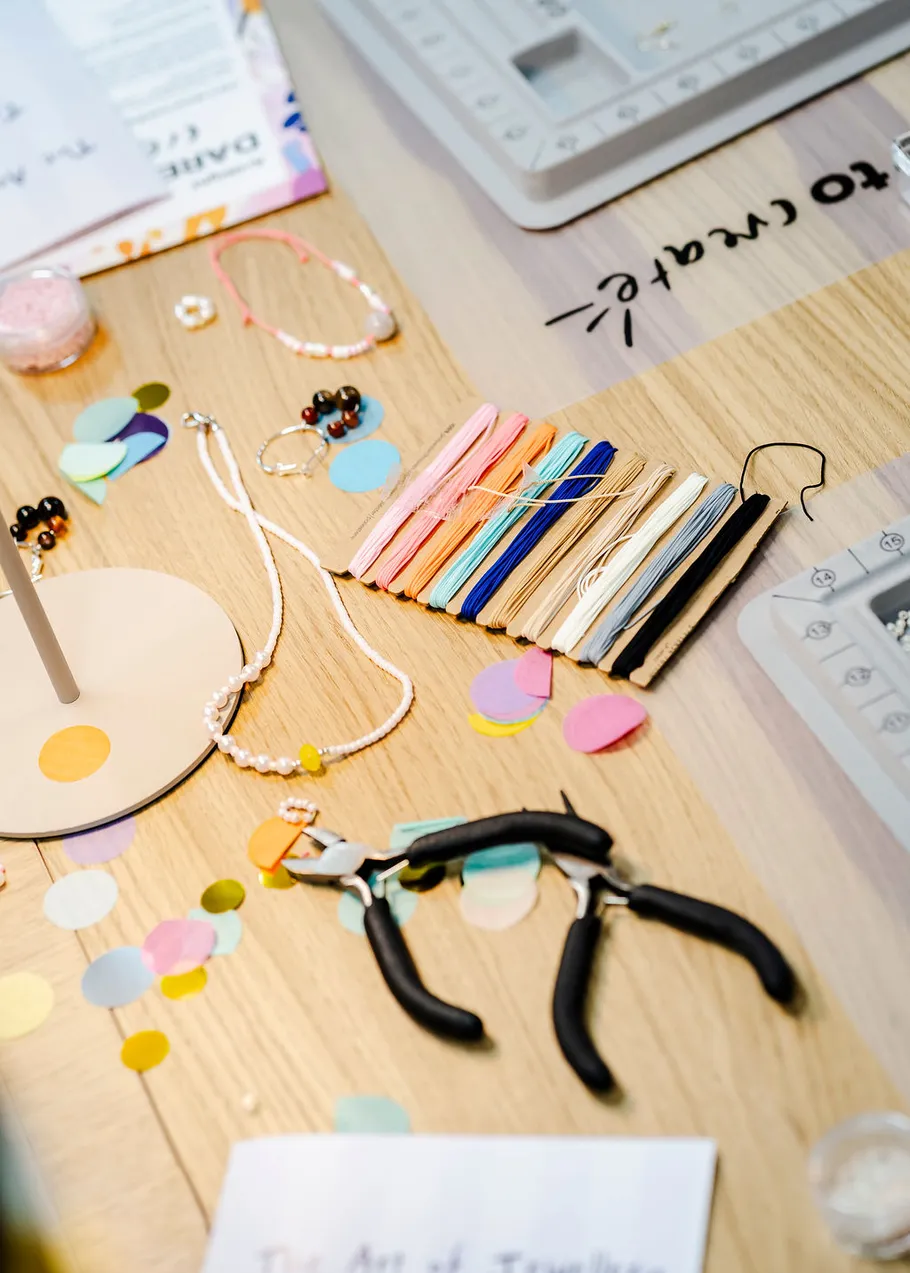 Jewelry-making tools and materials on wooden table.
