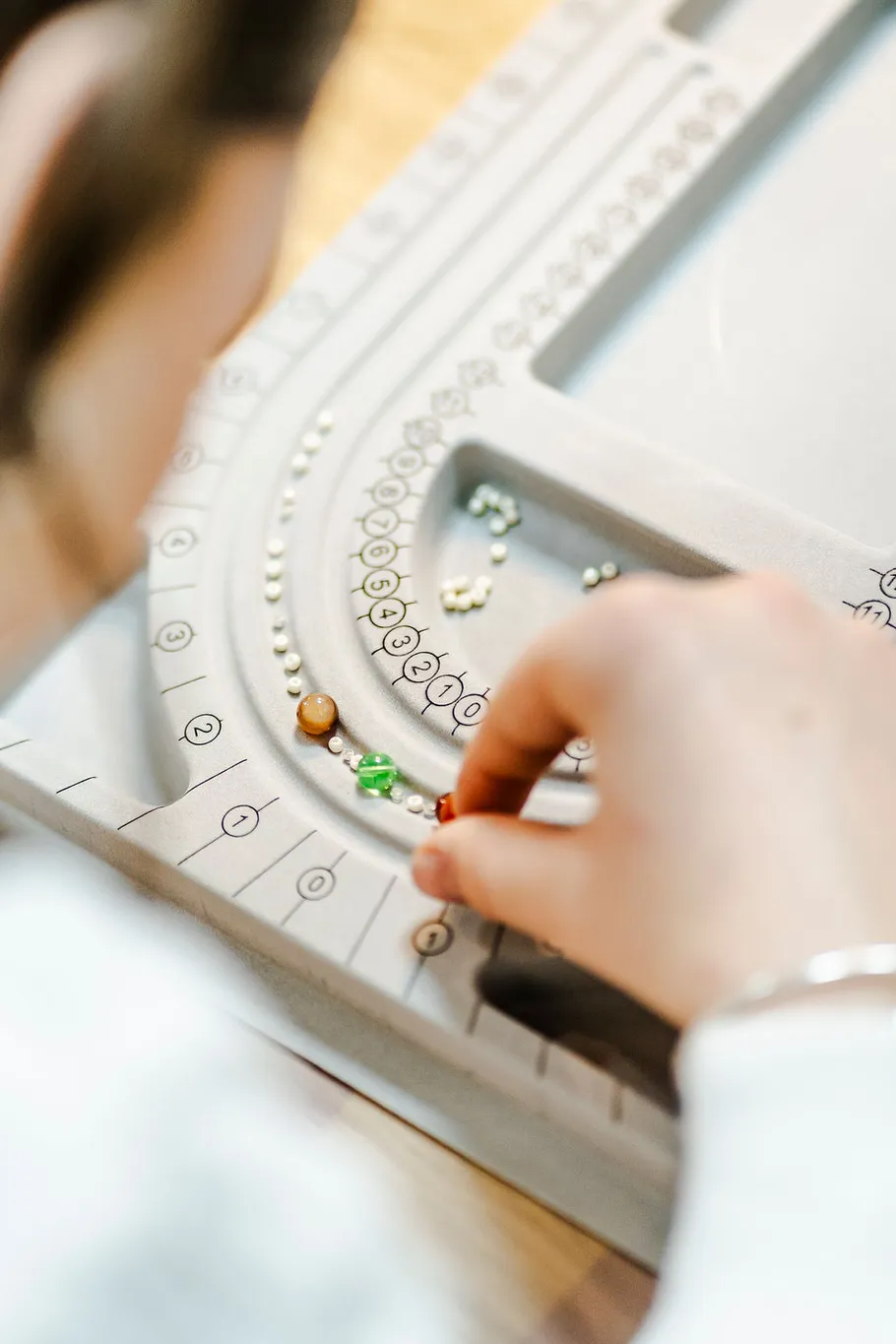 Person ordnet bunte Perlen auf Perlenbrett an.