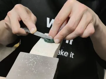 Hands cut a green stone on a block of wood.