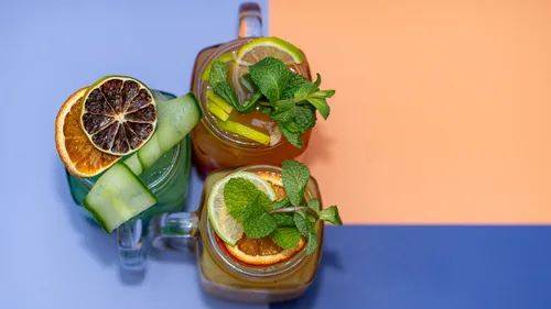 Three drinks with citrus and greens on table.