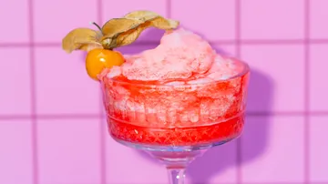 Pink cocktail with fruit garnish, tiled background.
