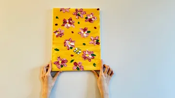 Hands holding floral painting on wall.