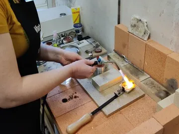 Person cutting and soldering with soldering torch in workshop.