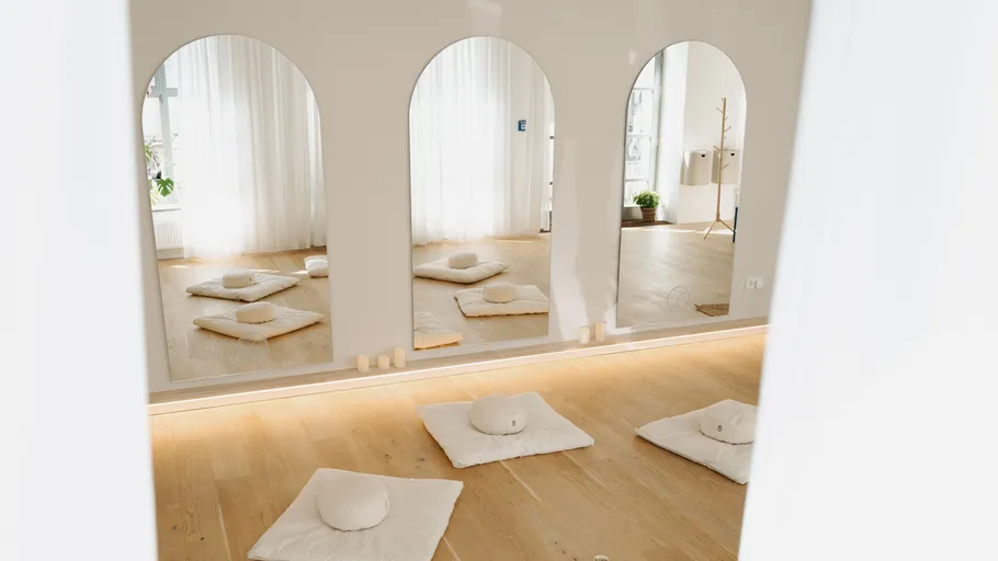 Meditation cushions on wooden floor, mirrored wall.