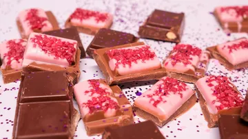 Schokoladenstücke mit rosa Himbeertopping auf Tisch.