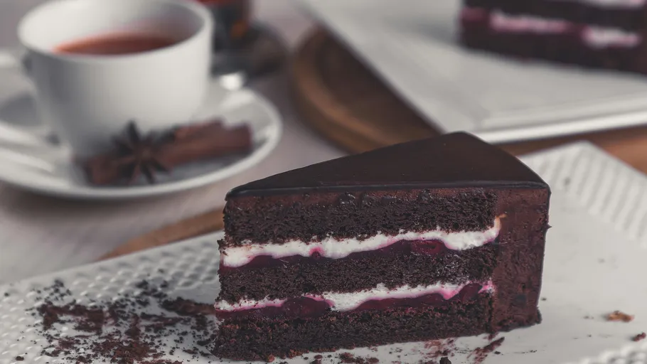 Schokoladenkuchenstück auf Teller, Tee im Hintergrund.