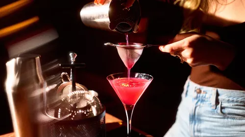 Person straining pink cocktail into glass.