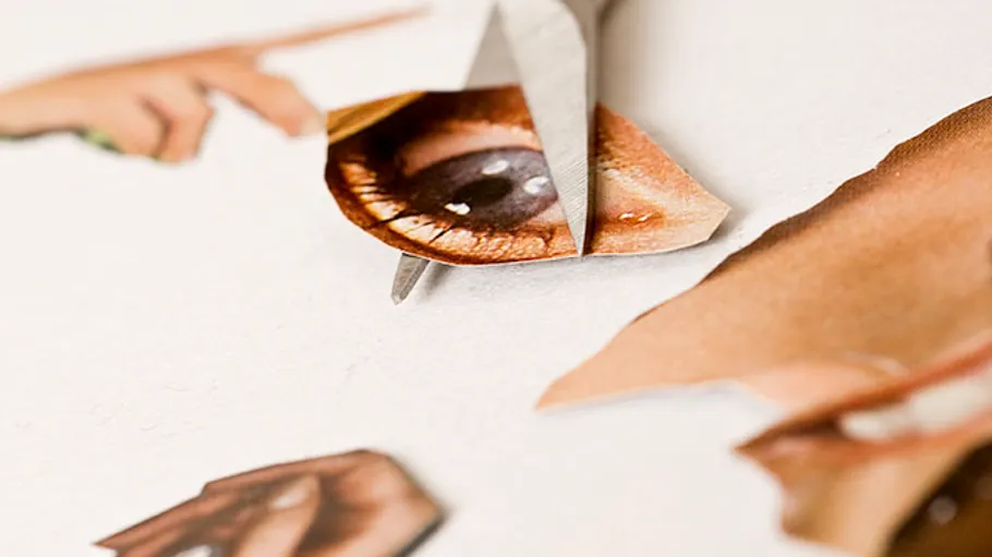 Scissors cutting out an eye from a magazine page.