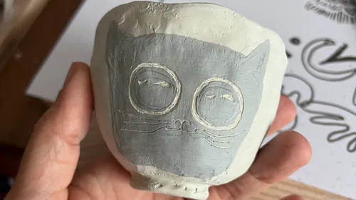 Hand hält kleinen Tongefäß mit Katzendesign.