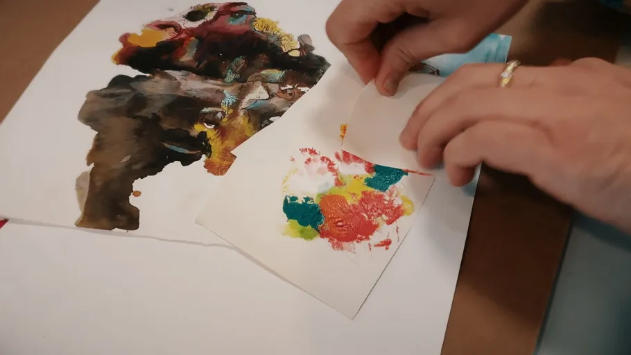 Hands peeling paper from colorful ink artwork.