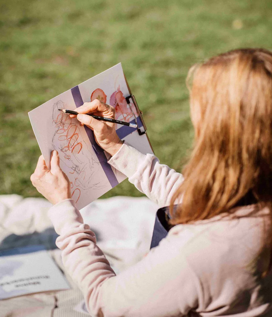Person zeichnet im Park auf Papier.