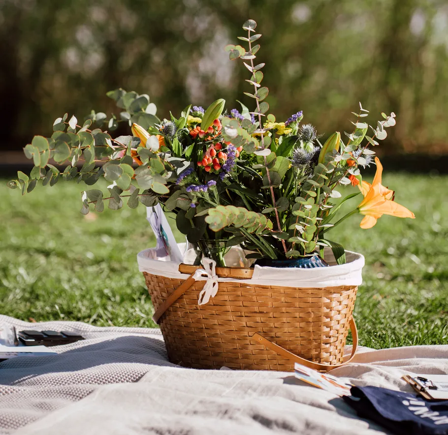 Basket with flowers on picnic blanket outside.