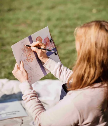 Person zeichnet im Freien auf Papier bei Sonnenschein.