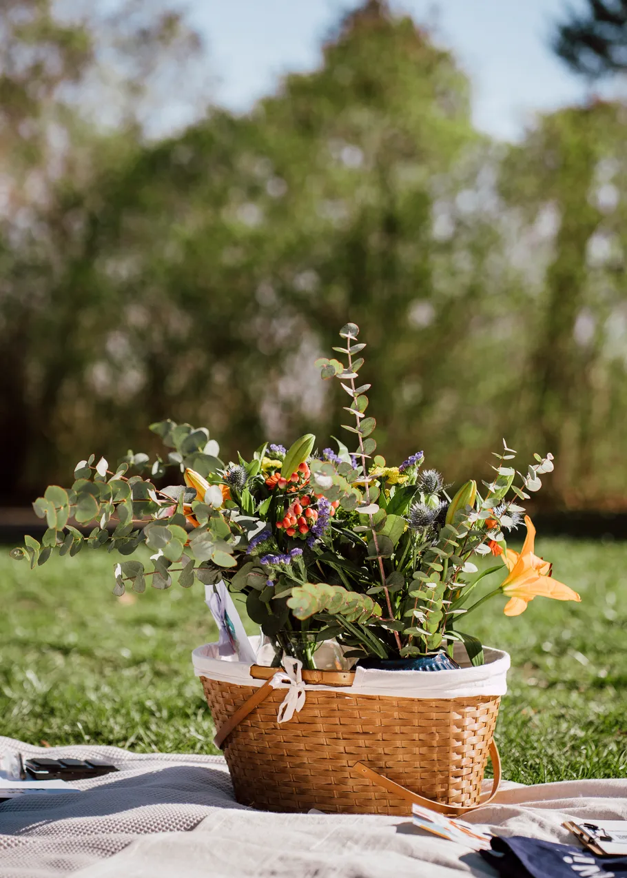 Basket with flowers on outdoor blanket.