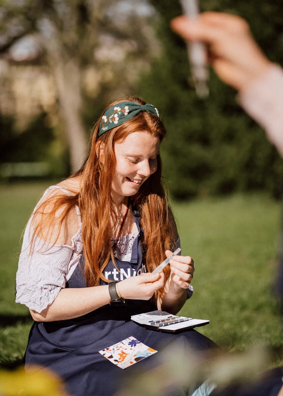 Woman smiling, painting in a sunny garden.