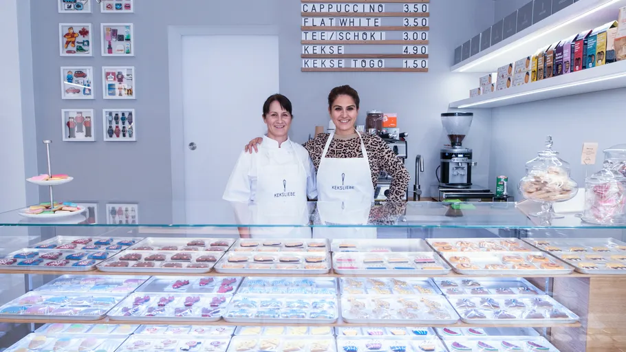 Two women behind bakery counter with pastries.