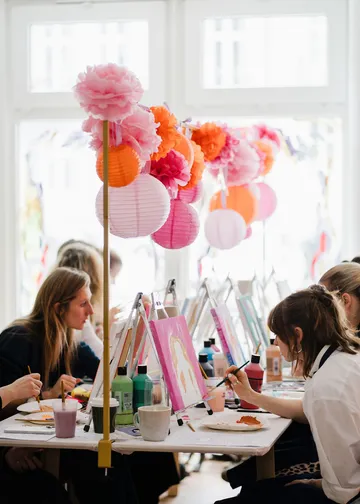 Women painting at tables with colorful decorations.