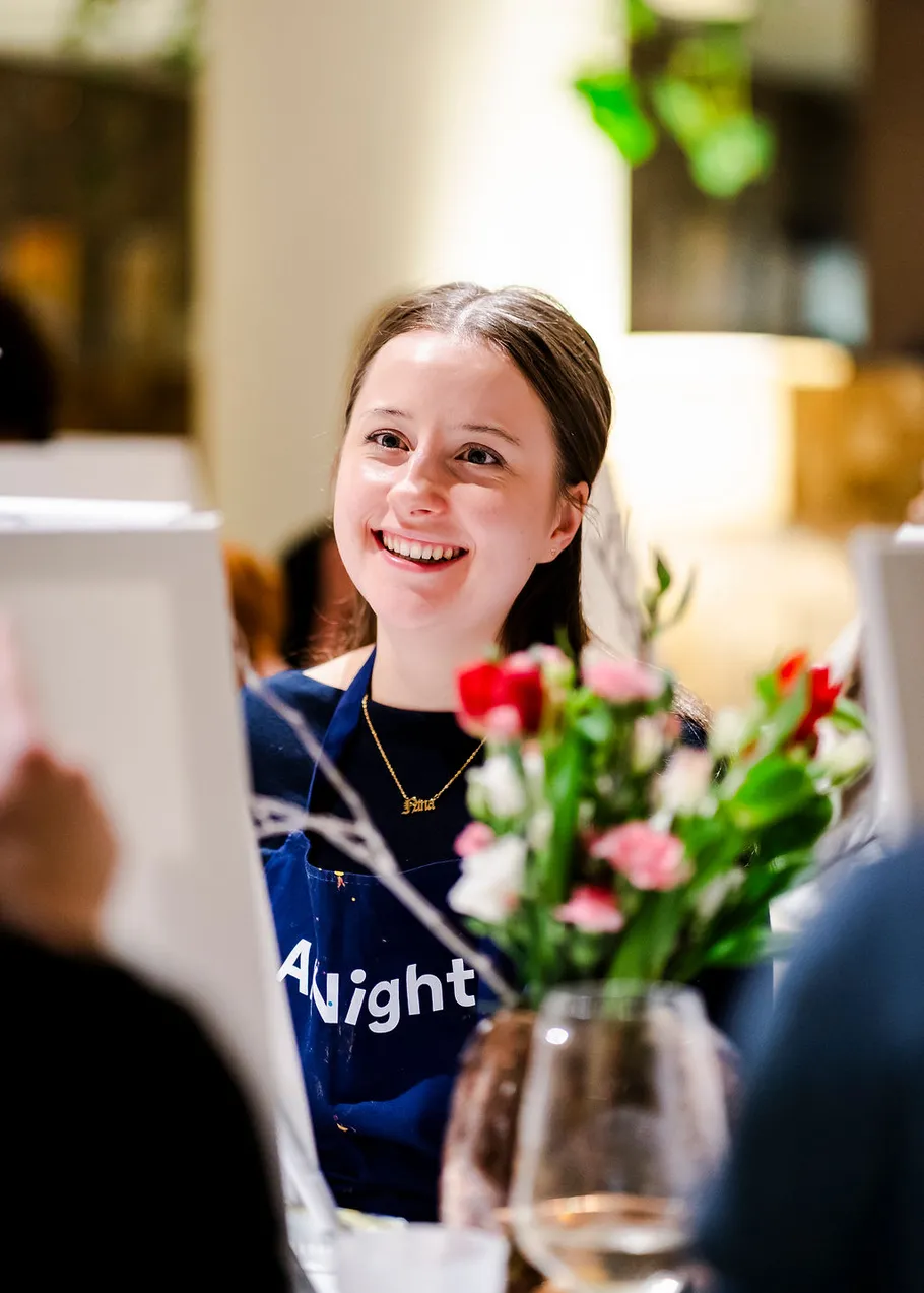 Smiling person painting in a social setting.